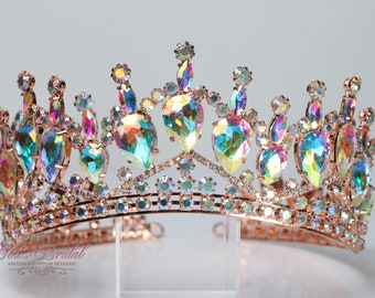 Puede incluir: Una corona de oro rosa con diamantes de imitación iridiscentes. La corona tiene una parte superior puntiaguda con un gran diamante de imitación en forma de lágrima en el centro. La corona está decorada con diamantes de imitación más pequeños alrededor de la base.