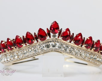 May include: A gold-toned tiara with a row of sparkling clear crystals and a row of large, teardrop-shaped, red gemstones. The tiara is set against a white background. The brand name "Yolis Bridal" is visible.