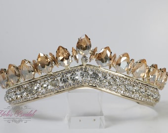 Puede incluir: Una tiara dorada con una fila de diamantes de imitación transparentes y una fila de cristales de color champán en forma de lágrima.