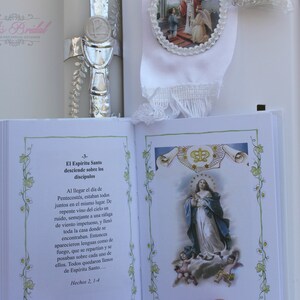May include: A white book with a green floral border and a picture of the Virgin Mary on the cover. The book has the text "El Espiritu Santo desciende sobre los discipulos" and "Hechos 2, 1-4" on the page.