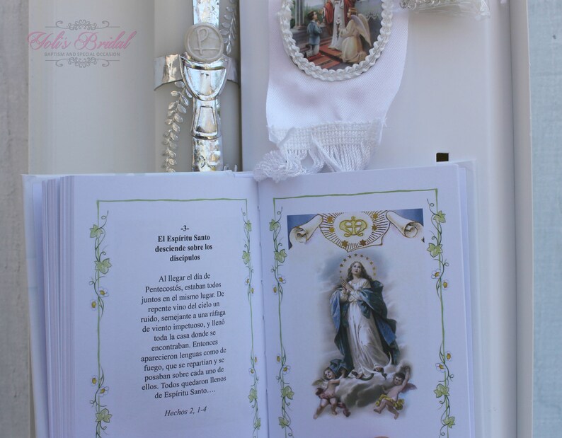 May include: A white book with a green floral border and a picture of the Virgin Mary on the cover. The book has the text "El Espiritu Santo desciende sobre los discipulos" and "Hechos 2, 1-4" on the page.