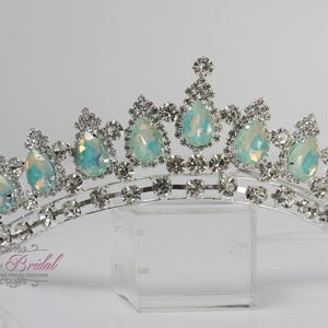 Könnte beinhalten: Silberfarbene Tiara mit schillernden, tropfenförmigen Steinen und klaren Kristallen. Die Tiara hat ein geschwungenes Design mit einem zentralen und kleineren Spitzen. Ein Brautaccessoire.