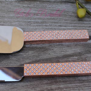 May include: A set of two cake cutting knives with rose gold handles and clear rhinestone embellishments.