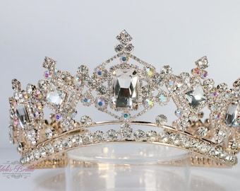 May include: A gold-toned tiara with clear and iridescent crystals. The crown features a central rectangular crystal and is adorned with numerous smaller, sparkling stones. The design is symmetrical and elegant, suitable for special occasions.