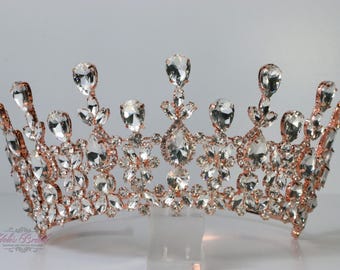 Puede incluir: Una corona de color oro rosa con cristales transparentes y brillantes. La tiara presenta un diseño simétrico con grandes cristales en forma de lágrima en los picos y cristales más pequeños en la base. Para ocasiones especiales.