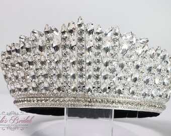 May include: A silver crown with a large number of clear rhinestones. The crown is on a black velvet base.