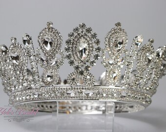 May include: A silver crown with a large, clear crystal center and smaller crystals surrounding it. The crown is decorated with intricate details and has a smooth, polished finish.