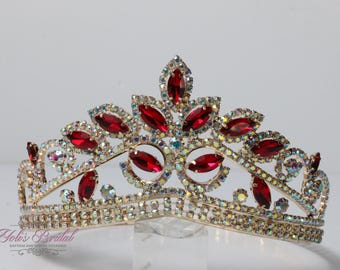 May include: A gold-toned tiara with red and iridescent gemstones. The crown features a symmetrical design with marquise-cut red stones and smaller, round iridescent gems. The base of the tiara is adorned with smaller, clear crystals.