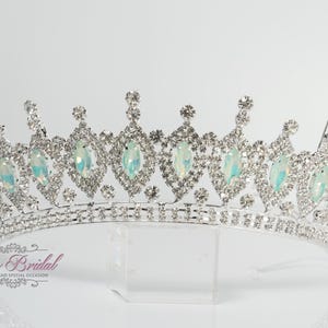 Peut inclure: Un diadème argenté orné de pierres précieuses claires et opalescentes. La couronne présente des motifs en forme de diamant avec des pierres opalescentes au centre. La base est bordée de petits gemmes clairs. Le diadème est conçu pour les occasions spéciales.