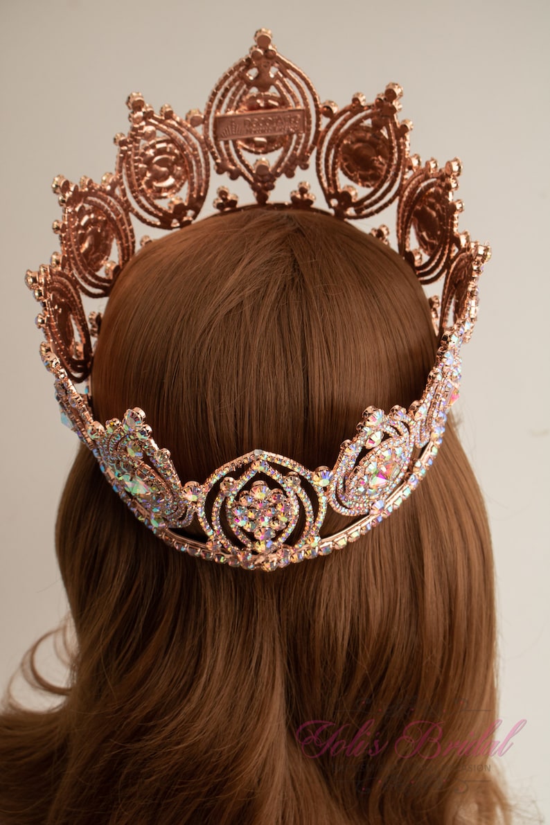 May include: A rose gold crown with clear iridescent rhinestones. The crown is made of metal and has a delicate design.