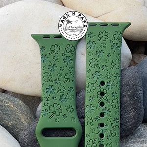 May include: Green Apple Watch band with a clover pattern. The band is made of silicone and features a repeating design of shamrocks. The band has the text "Wags N Pawz" in a circular logo.