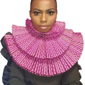 May include: A pink ruffled collar with a floral pattern. The collar is layered and stands out against a black garment. The design is intricate and eye-catching, suitable for special occasions or costume wear.