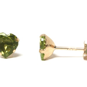 May include: A pair of gold heart shaped earrings with green gemstones. The earrings are on a white background.