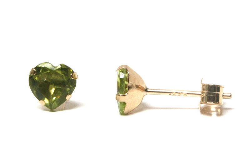 May include: A pair of gold heart shaped earrings with green gemstones. The earrings are on a white background.