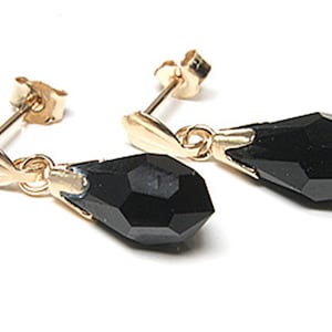 May include: A pair of gold earrings with black teardrop-shaped crystals hanging from them.