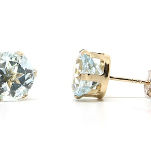 Puede incluir: Un par de pendientes de oro con piedras preciosas de aguamarina azul claro. Los pendientes tienen forma redonda y están engastados en garras.