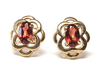 May include: A pair of gold earrings with red gemstone accents. Each earring features a delicate flower design with a red oval-shaped gemstone in the centre.