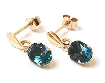 Puede incluir: Un par de pendientes de oro con piedras preciosas ovaladas azules que cuelgan de la parte inferior. Los pendientes tienen un diseño sencillo y son perfectos para el uso diario.
