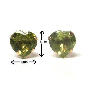 May include: Two heart shaped green peridot earrings with gold settings. The earrings are 5mm in diameter.