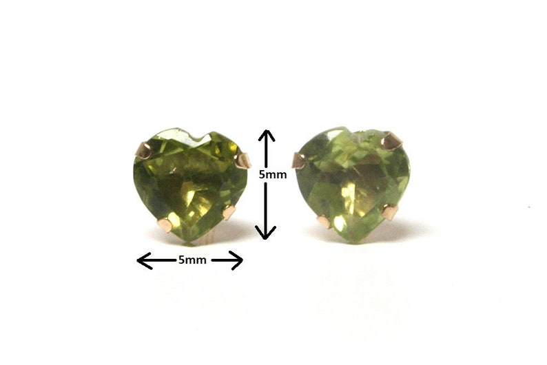 May include: Two heart shaped green peridot earrings with gold settings. The earrings are 5mm in diameter.