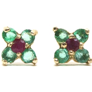 May include: A pair of gold earrings with a flower design. Each earring has five green emeralds and one red ruby in the center.