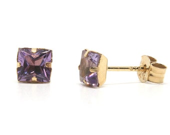 May include: A pair of gold stud earrings with square purple gemstones.