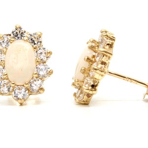 May include: A pair of gold earrings featuring a white opal gemstone set in a halo of smaller clear gemstones.