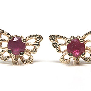 May include: A pair of gold butterfly earrings with red ruby gemstones in the center of each butterfly.
