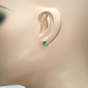 Puede incluir: Primer plano de la oreja de un maniqu&iacute; con un peque&ntilde;o pendiente redondo de piedra preciosa verde.
