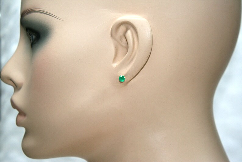 Puede incluir: Primer plano de la oreja de un maniqu&iacute; con un peque&ntilde;o pendiente redondo de piedra preciosa verde.