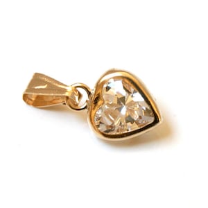 May include: A gold heart-shaped pendant with a clear crystal in the centre. The pendant has a bail for attaching to a chain.