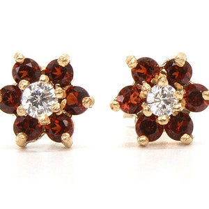 May include: A pair of gold flower-shaped earrings with a clear centre stone and red gemstones around it.