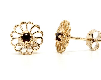 May include: A pair of gold earrings featuring a delicate flower design with a small red gemstone at the centre.