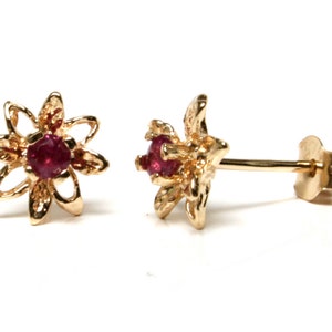 May include: A pair of gold flower-shaped earrings with red gemstones in the centre.