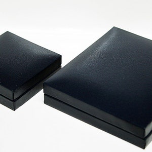 Może przedstawiać: Dwa czarne pudełka prezentowe, jedno nieco większe od drugiego, pokazane na białym tle. Pudełka wykonane są z fakturowanego materiału i mają gładką, płaską g&oacute;rę.