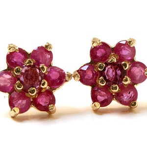 May include: A pair of gold earrings with ruby flower designs. Each earring features a cluster of red rubies set in a star shape.