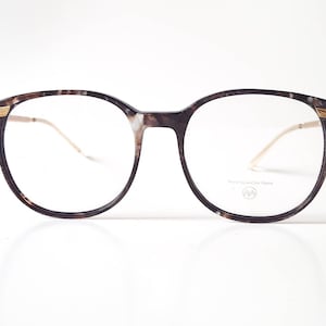 May include: Brown tortoise shell eyeglasses with gold accents and clear lenses. The glasses have a round frame and are made of plastic.