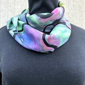 May include: A silk scarf with a colorful abstract design in shades of pink, purple, green, and blue. The design features black lines and swirls.