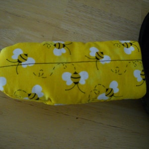 May include: Yellow oven mitt with a bee pattern. The mitt is made of fabric and has a quilted design.