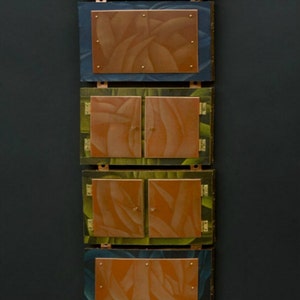 May include: A vertical wall sculpture made of wood and metal with a series of rectangular and arched panels. Each panel features a different color and a design of stylized leaves. The panels are connected by metal hinges and have a copper finish.