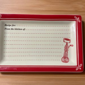May include: Rectangular ceramic recipe dish with a red border and a cream-colored interior. The dish features the text "Recipe for:" and "From the kitchen of:" with dashed lines for writing. A red illustration of a vintage egg beater is on the right.