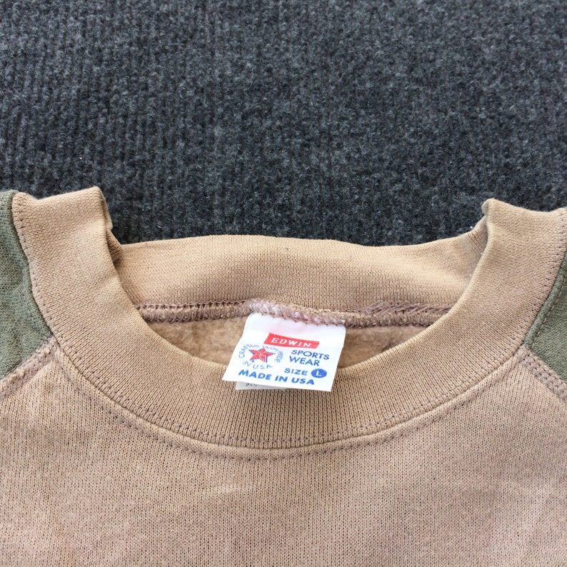 Op de afbeelding: Tan sweatshirt met groene raglanmouwen. De sweatshirt heeft een ronde hals en een label met de tekst "Edwin Sports Wear Maat L Gemaakt in de VS".