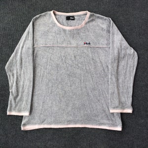 Puede incluir: Camiseta gris de manga larga con ribete rosa alrededor del cuello y el dobladillo inferior. La camiseta tiene la palabra "FILA" en letras negras en la parte delantera.