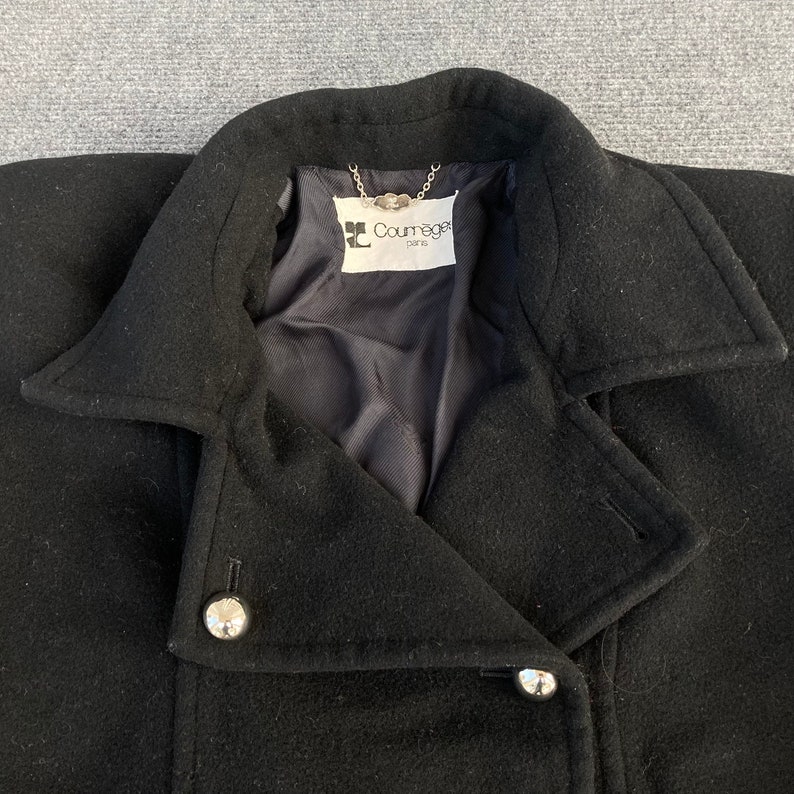 May include: Black wool coat with a notched collar and silver-tone buttons. The coat features a double-breasted design and a label that reads "Courr&egrave;ges Paris". The coat is a classic outerwear piece.