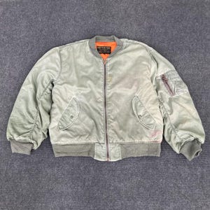 May include: A green bomber jacket with a zip fastening and a patch on the left sleeve that says "Airman's Gear".