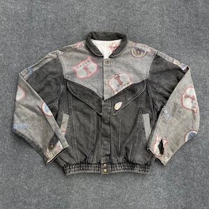 Pode incluir: Uma jaqueta jeans vintage em tons de cinza e preto, com um design exclusivo de patches e gráficos estampados. A jaqueta tem uma frente abotoada, bolsos e uma bainha canelada. Os patches incluem o texto "MAJOR" e "I MOTEL".