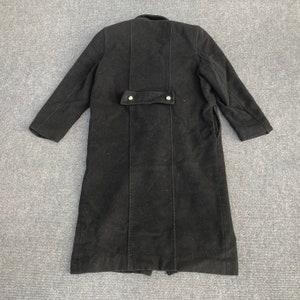 May include: A long, black coat with a buttoned back detail and a notched collar. The coat has long sleeves and a tailored fit, suitable for colder weather. The coat is made of a thick, dark fabric.