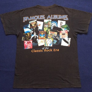 May include: Black t-shirt with a collage of album covers from the "Classic Rock Era". The text "Famous Albums" is at the top of the collage.