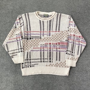 May include: A cream-colored sweater with a geometric pattern in black, brown, red, and purple. The sweater has a crew neck and long sleeves.