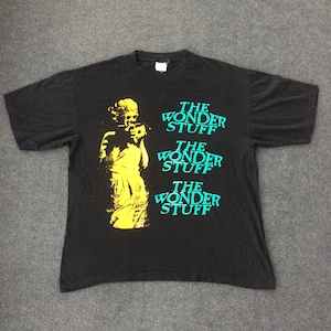 Puede incluir: Camiseta negra con una imagen amarilla de una mujer sosteniendo una cámara y el texto "The Wonder Stuff" repetido tres veces en verde azulado y amarillo.